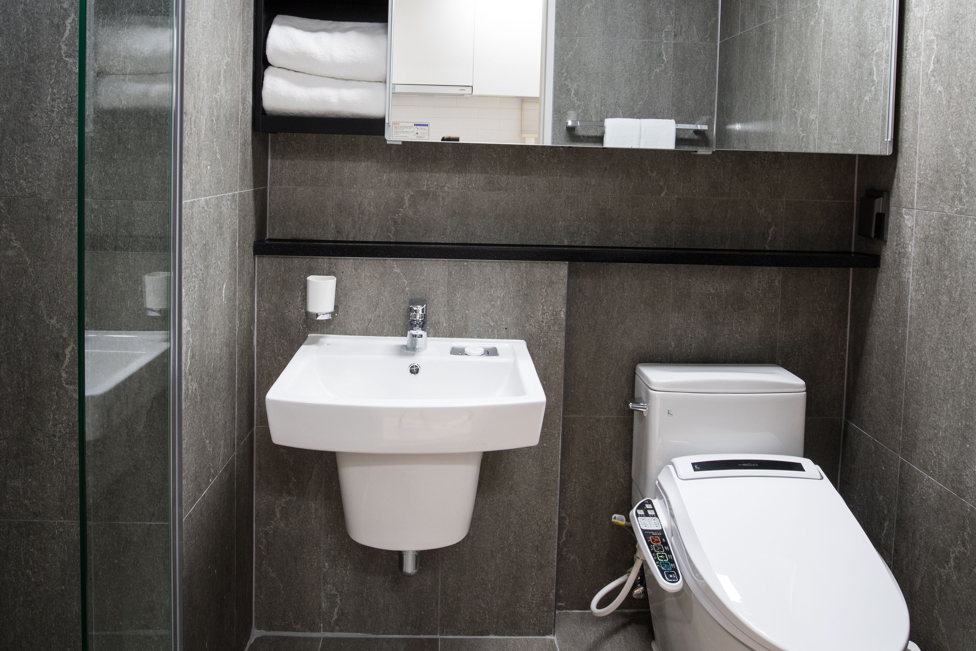 A modern bathroom with a glass shower enclosure, a white sink, and a toilet with a control panel.