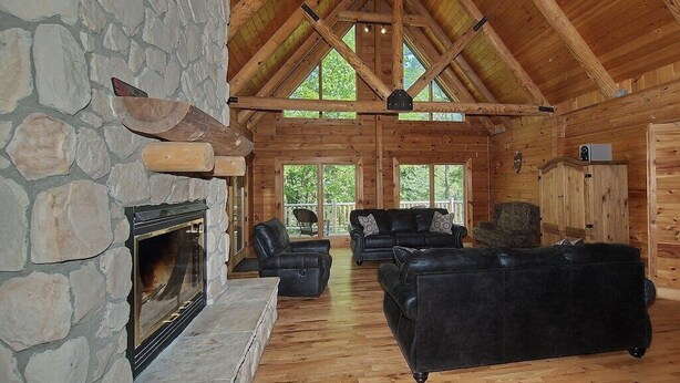 A log cabin interior with a stone fireplace, wooden ceiling beams, and a stone wall. - Spacious 8-Bedroom Retreat at Martinwoods Cabins, Perfect for family gatherings (Rockbridge)