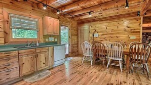 A wooden cabin interior with a kitchen and dining area, featuring wooden floors, cabinets, and a dining table with chairs. - Spacious 8-Bedroom Retreat at Martinwoods Cabins, Perfect for family gatherings (Rockbridge)