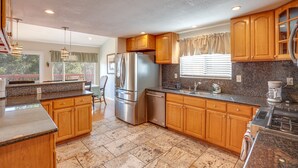 Una cocina con armarios de madera, encimeras de granito, electrodomésticos de acero inoxidable y una ventana con cortinas.