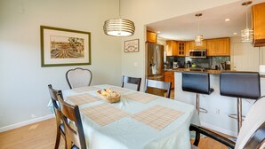 Un comedor con una mesa dispuesta para cuatro, una cocina al fondo y un cuadro en la pared.