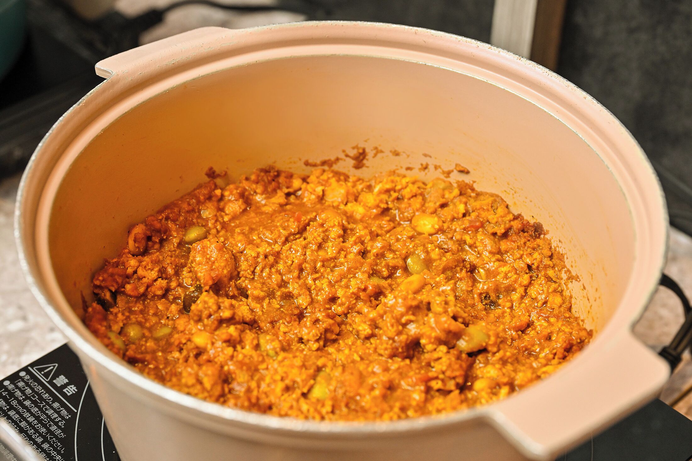 Una olla grande llena de un guiso espeso de color naranja, posiblemente un curry o estofado, colocada sobre una encimera de cocina.