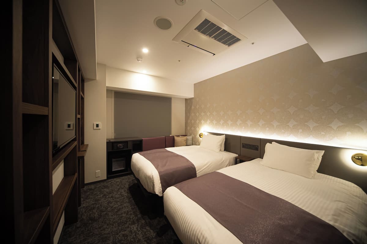 A hotel room with two beds, a wardrobe, a desk, and a mirror.