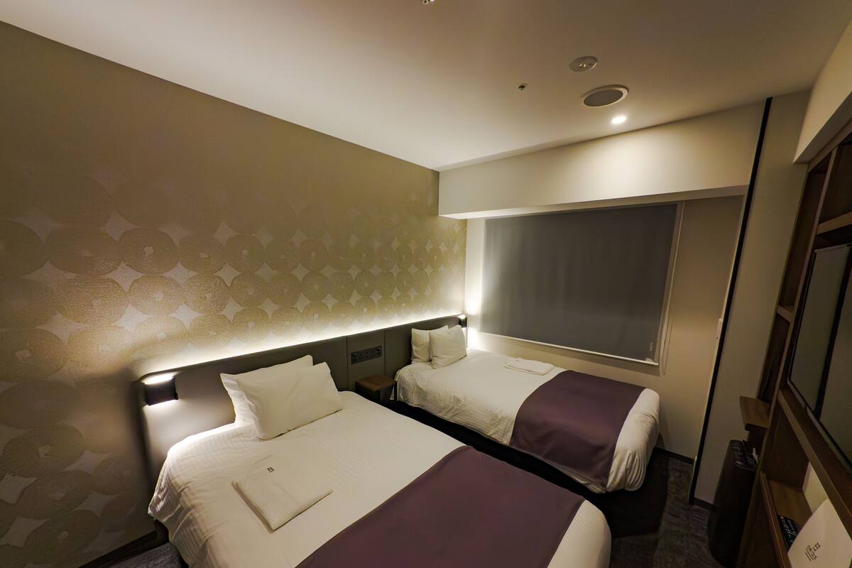 A hotel room with two beds, a large window, and a mirror.