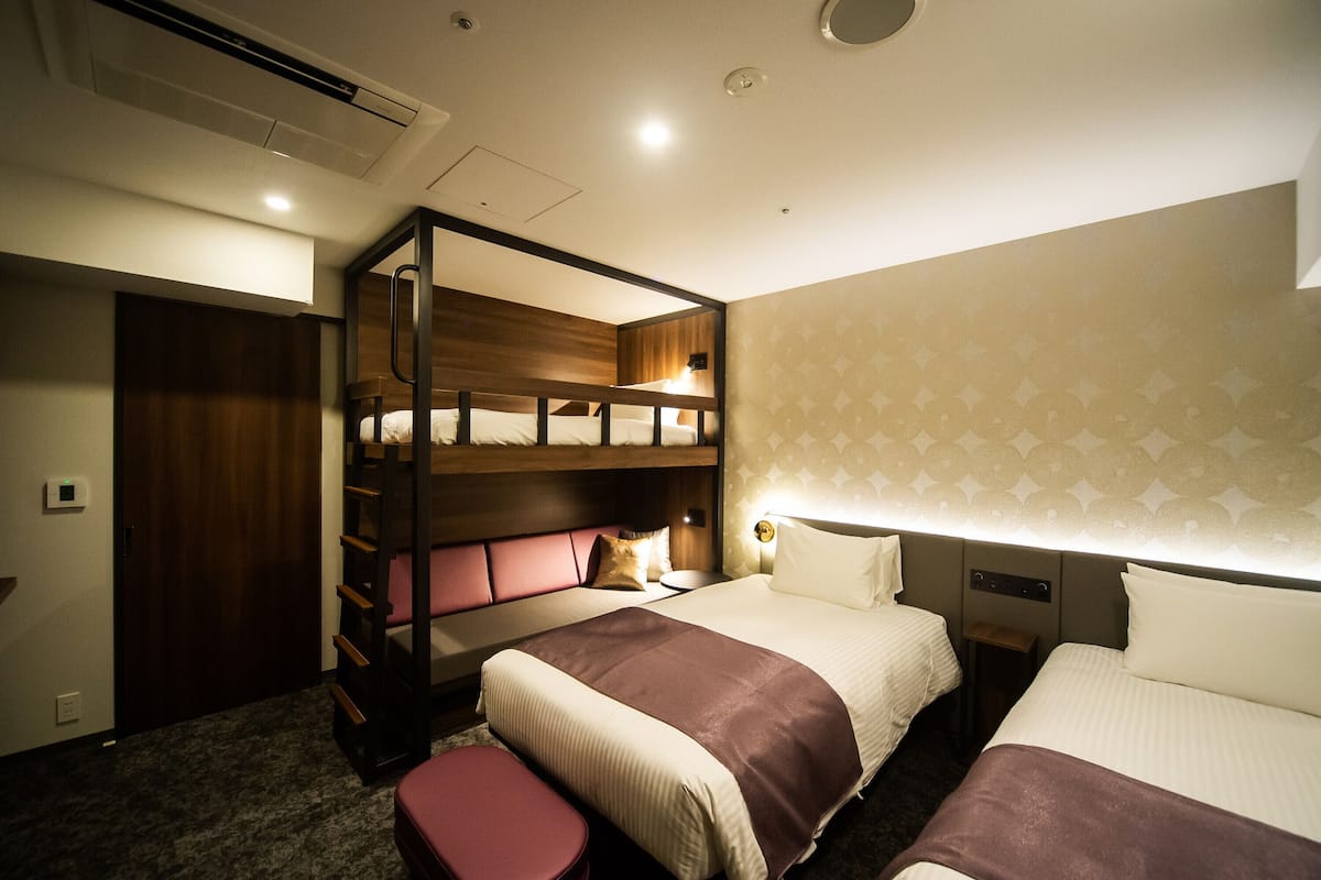 A hotel room with bunk beds, a desk, and a small stool.
