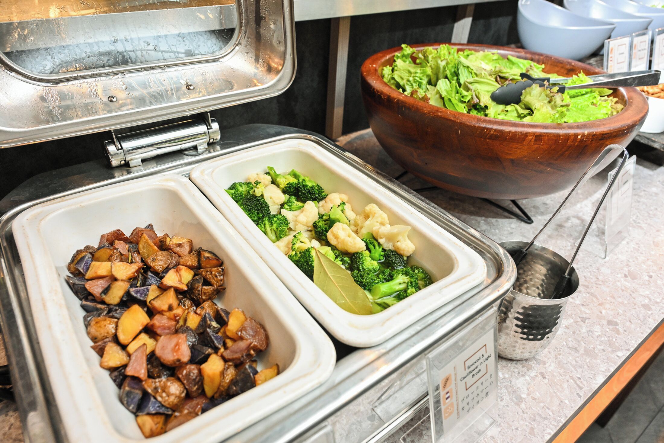 A buffet with various dishes including roasted vegetables and a large salad bowl.