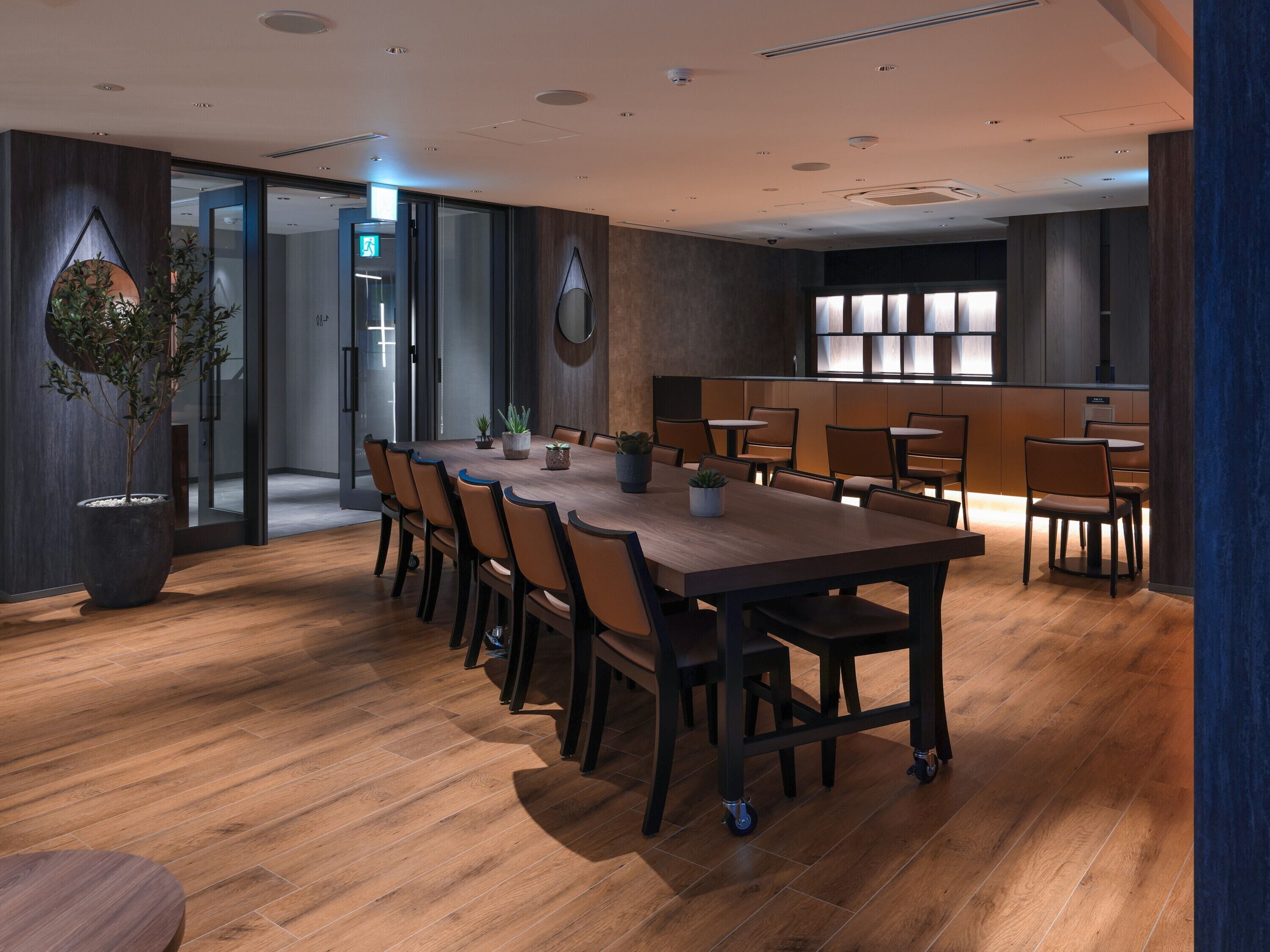 A modern conference room with a large wooden table, chairs, and potted plants.