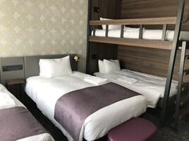 A hotel room with a bunk bed, a single bed, a nightstand, and a wall-mounted light fixture.