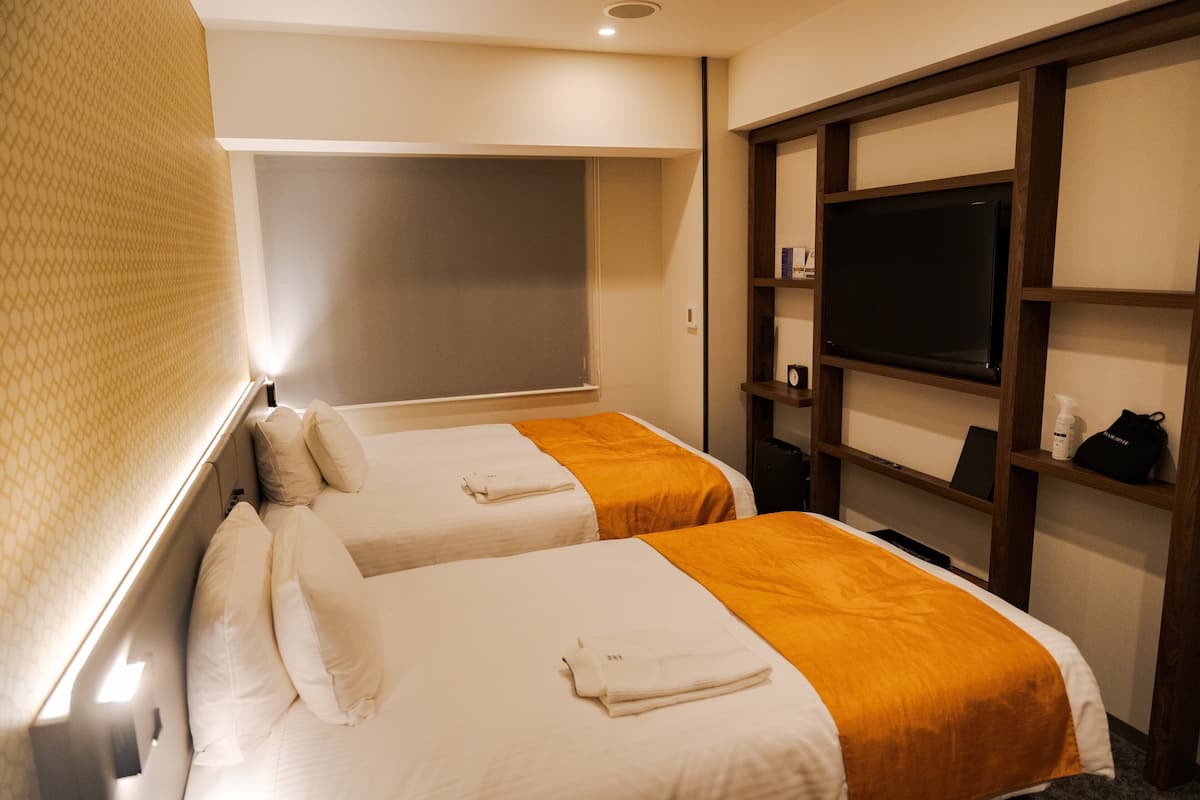A hotel room with two beds, a television, and a shelf with toiletries.