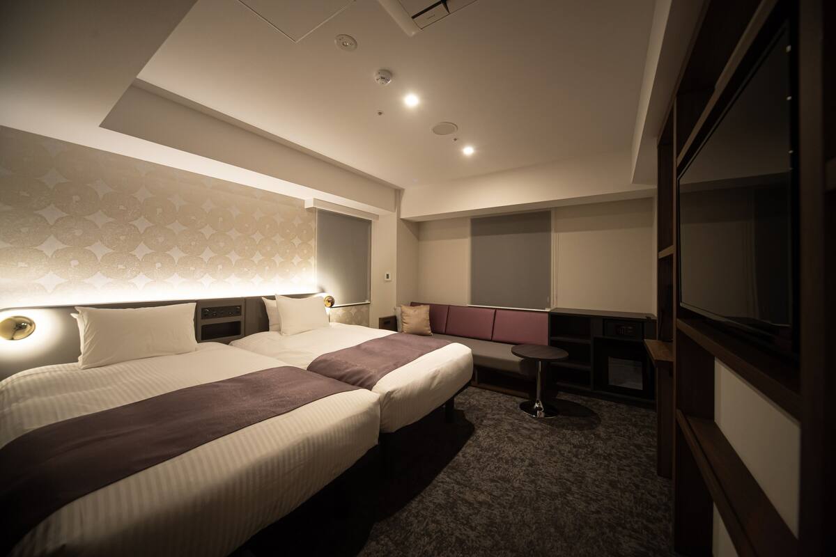 A hotel room with two beds, a small seating area, a television, and a minibar.