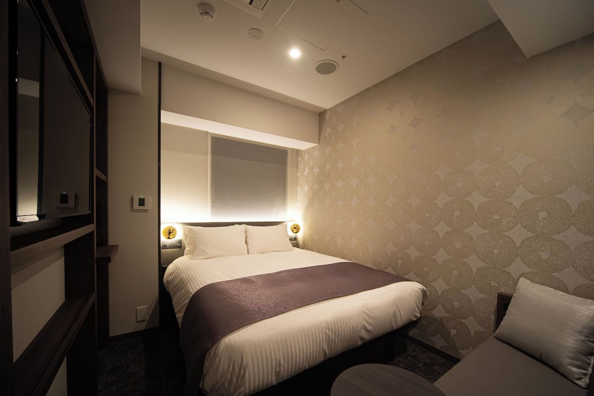 A hotel room with a bed, bedside tables, a mirror, and a patterned wall.