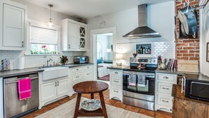 A modern kitchen with white cabinets, a stainless steel range, and a brick accent wall. - Cultural district bungalow steps from Dickies arena (Fort Worth)