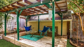 A covered patio with a wooden deck, two blue folding chairs, a glass table, and a hanging light fixture. - Cultural district bungalow steps from Dickies arena (Fort Worth)