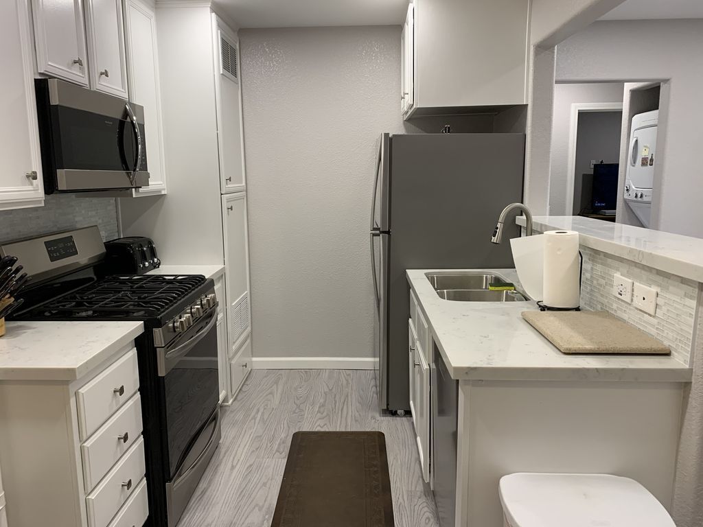 A compact kitchen with white cabinets, a stainless steel refrigerator, a microwave, a stove, and a sink.