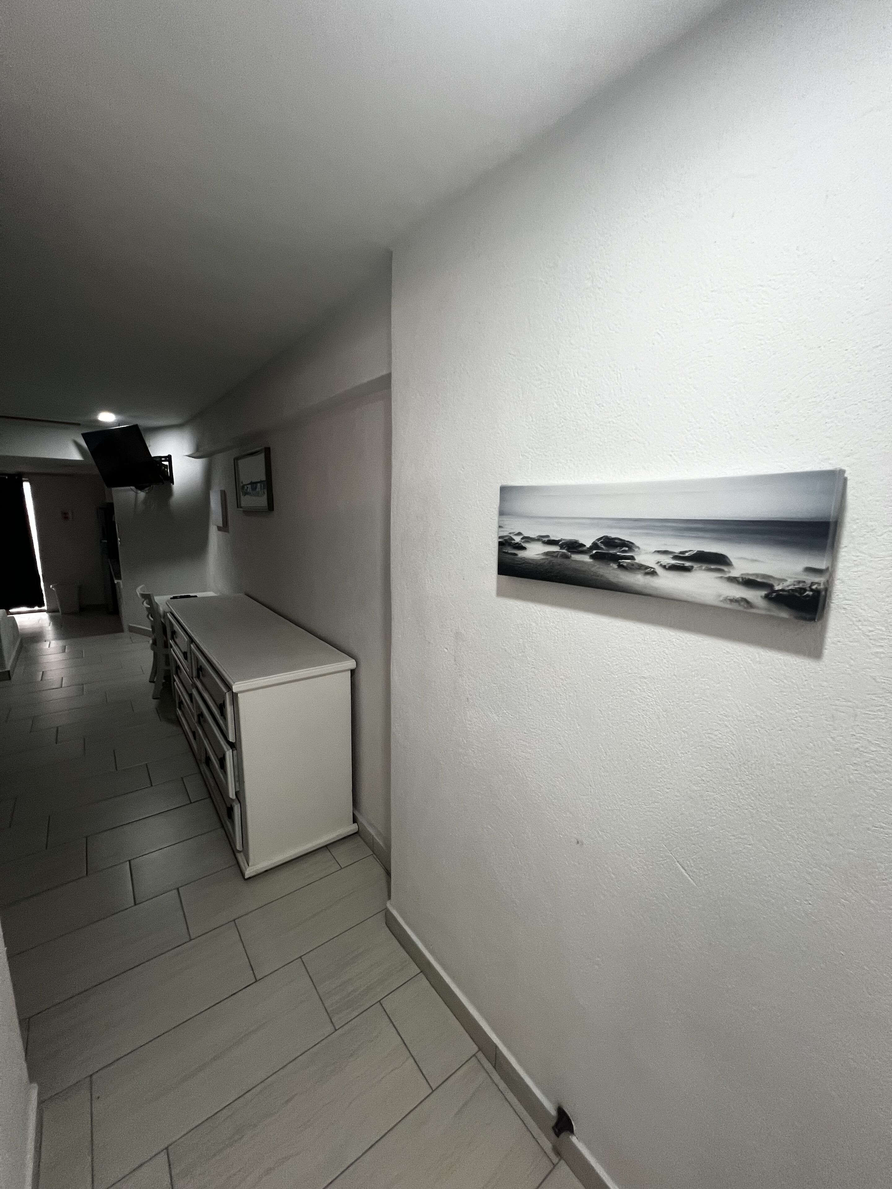 Een gang met een witte kast, een flatscreentelevisie aan de muur en een lijst met een foto van een strand.