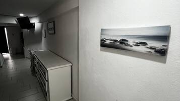 Een gang met een witte kast, een flatscreentelevisie aan de muur en een lijst met een foto van een strand.