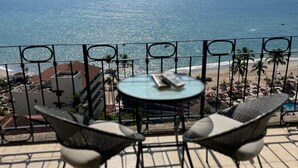 Une terrasse avec une table ronde et deux chaises, donnant sur une plage et la mer.