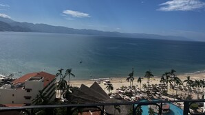 Une vue sur la plage, avec une piscine, des palmiers et un ciel dégagé.