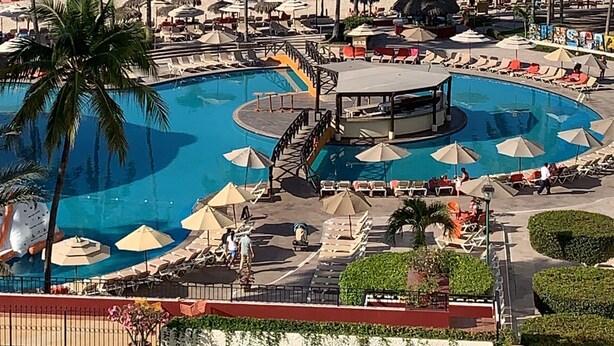 Un complexe hôtelier doté d’une grande piscine, de palmiers et offrant une vue sur l’océan.