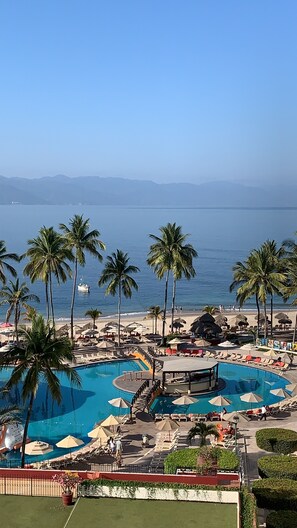 Un resort con una amplia piscina, palmeras y vistas al océano.