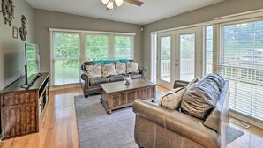 A spacious living room with a ceiling fan, a dark brown leather sofa, a wooden coffee table, and a large window with blinds. - 7 Mi to Nat'l Park: Home w/ Dock in Hot Springs (Hot Springs)
