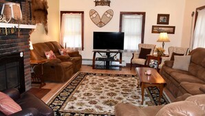 A living room with a fireplace, leather sofas, a flat-screen TV, and decorative wall art. - Adirondack Big Pines- House sleeps 12 (Caroga Lake)