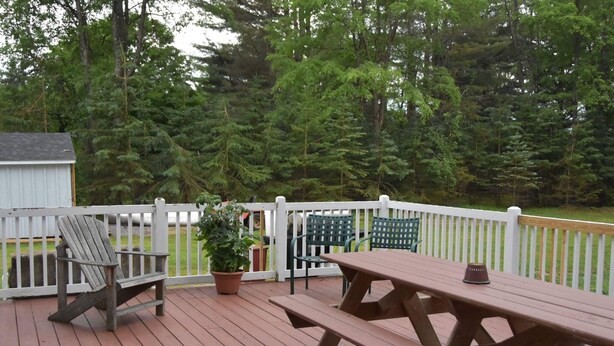 A wooden deck with a picnic table and chairs, surrounded by a white fence and a view of a forested area. - Adirondack Big Pines- House sleeps 12 (Caroga Lake)