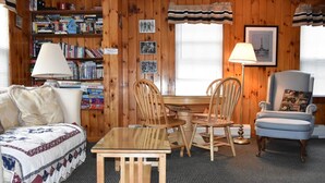 A cozy cabin interior with a wooden bookshelf, a dining table with chairs, a blue armchair, and a quilted sofa. - Adirondack Big Pines- House sleeps 12 (Caroga Lake)