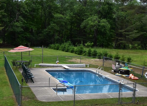 A rectangular pool with a diving board and a slide, surrounded by a fence.