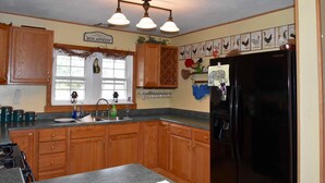 A kitchen with wooden cabinets, a black refrigerator, a sink, and a window with a view of greenery outside. - Adirondack Big Pines- House sleeps 12 (Caroga Lake)