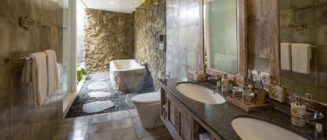 A modern bathroom with a stone wall, a bathtub, two sinks, and a large mirror.