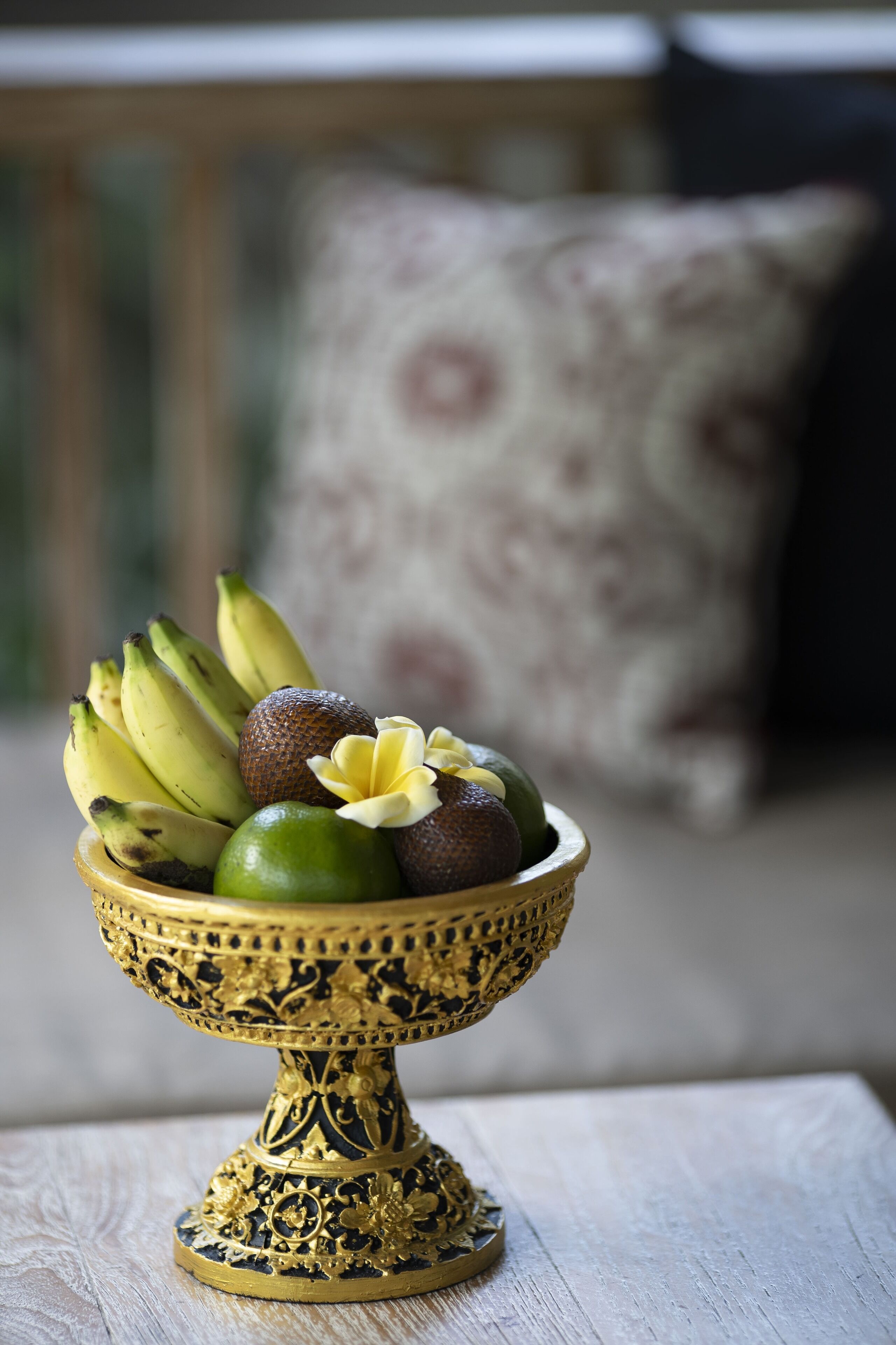 A decorative bowl with fruits and a flower on a wooden table.