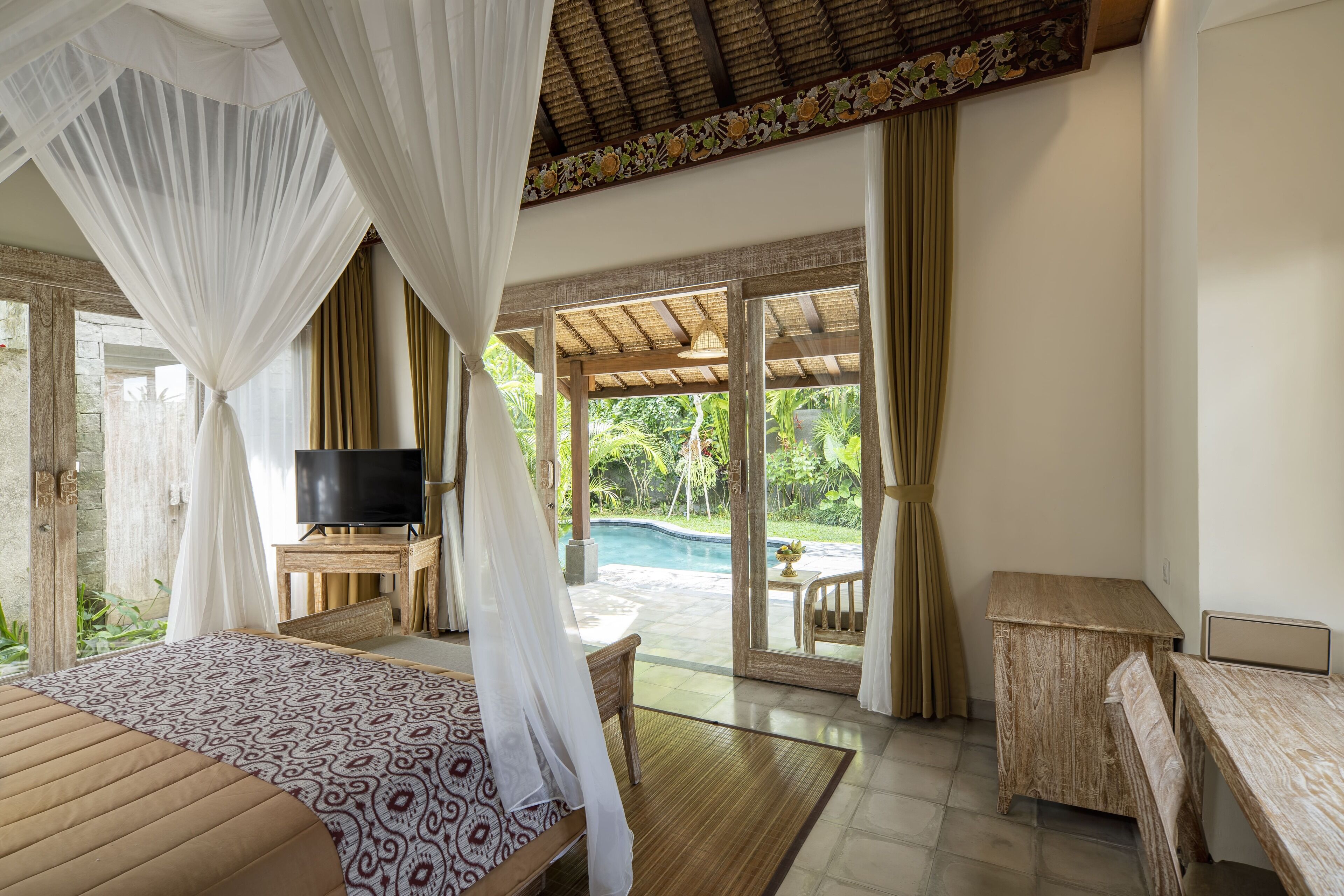 Quarto com cama, TV e vista para a piscina e jardim.