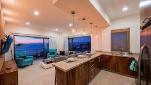 A modern kitchen with a large island, a dining area with a view, and a living room with a sofa and chairs. - Nise (Puerto Vallarta)