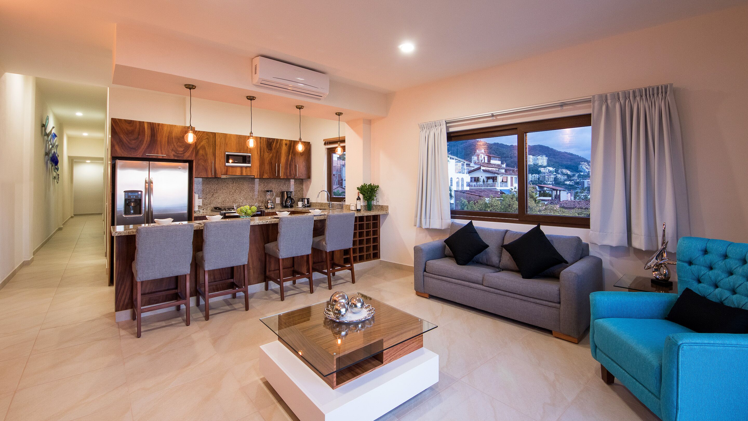 A modern living room with a sofa, a coffee table, and a view of a cityscape through large windows.