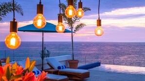A seaside lounge with hanging light bulbs, a blue umbrella, and a view of the ocean. - Nise (Puerto Vallarta)
