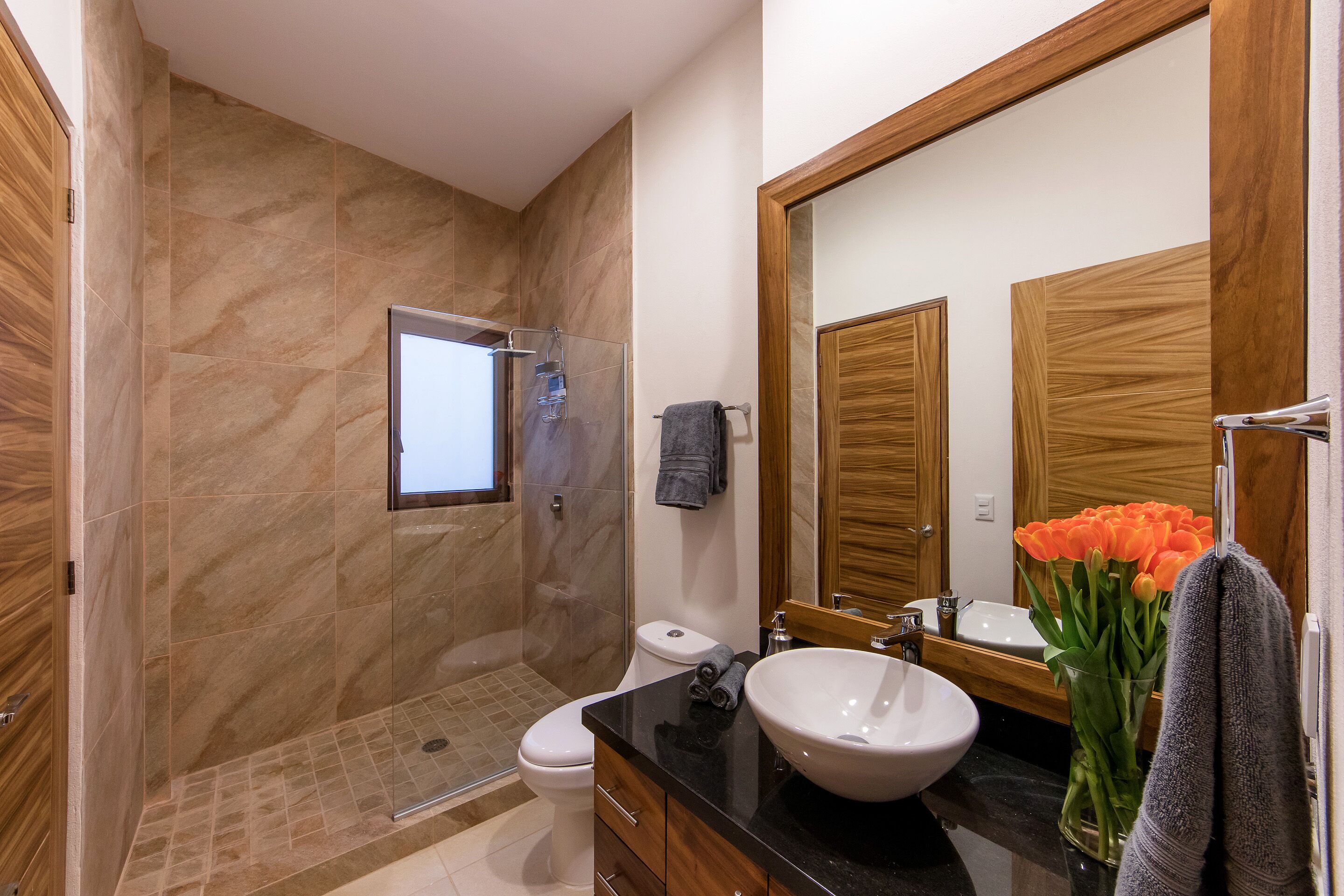 A modern bathroom with a glass-enclosed shower, a white sink, and a large mirror.