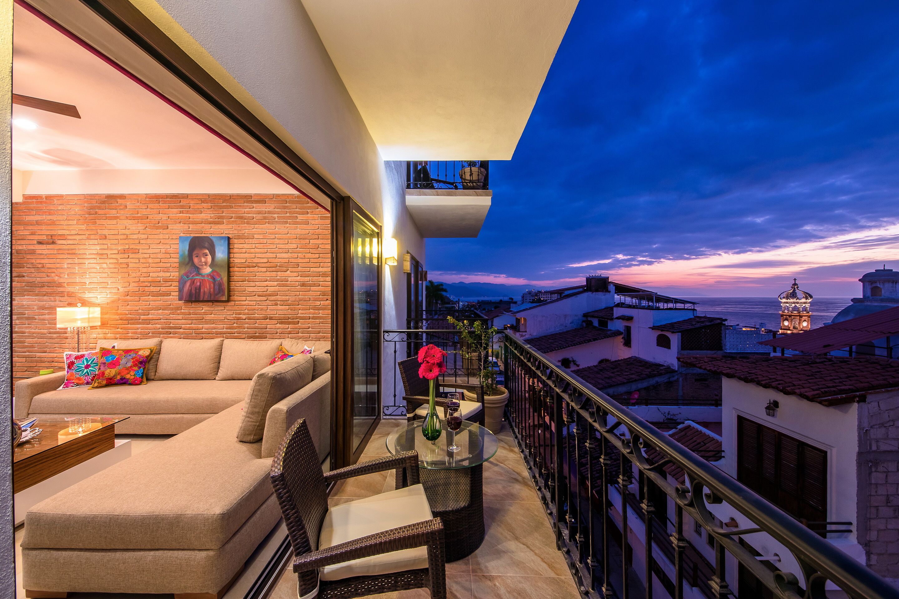 A balcony with a sofa, chairs, a table, and a vase of flowers.