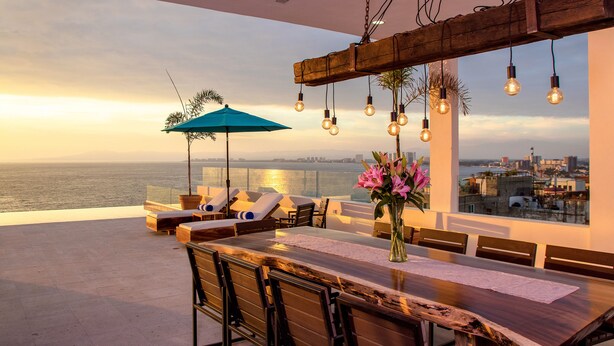 A rooftop terrace with a wooden dining table, lounge chairs, and a view of the city and sea. - Nise (Puerto Vallarta)