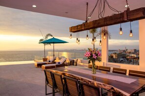 A rooftop terrace with a wooden dining table, lounge chairs, and a view of the city and sea. - Nise (Puerto Vallarta)