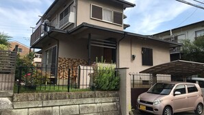 A two-story residential building with a balcony, a car parked in front, and a small garden area. - Bonel Guest House (Tomisato)