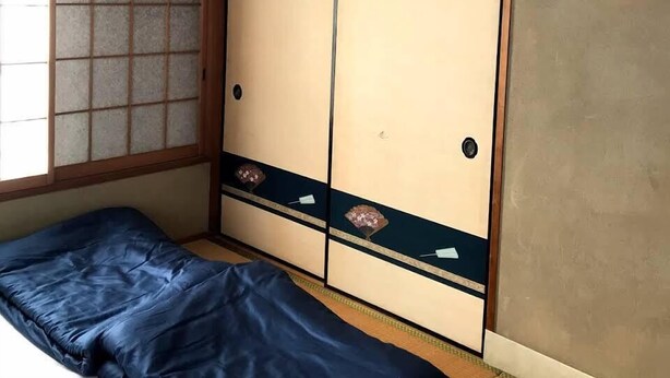 A traditional Japanese room with tatami flooring, a low wooden bed, sliding shoji doors, and a view of a garden through a shoji screen. - Bonel Guest House (Tomisato)