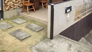 A house with a tiled patio, two wooden chairs, a small table, and a door leading inside. - Bonel Guest House (Tomisato)