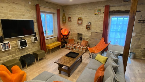 A cozy living room with a stone wall, a large flat-screen TV, a fireplace, and comfortable seating including a sofa and armchairs.