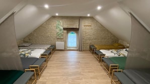 A spacious attic room with two beds, wooden benches, a stone wall, and a window with curtains.