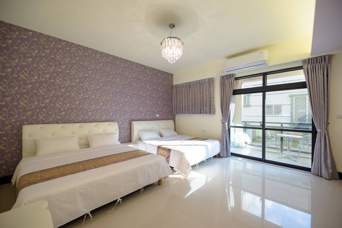 A hotel room with two beds, a chandelier, an air conditioning unit, and a view of the outside.
