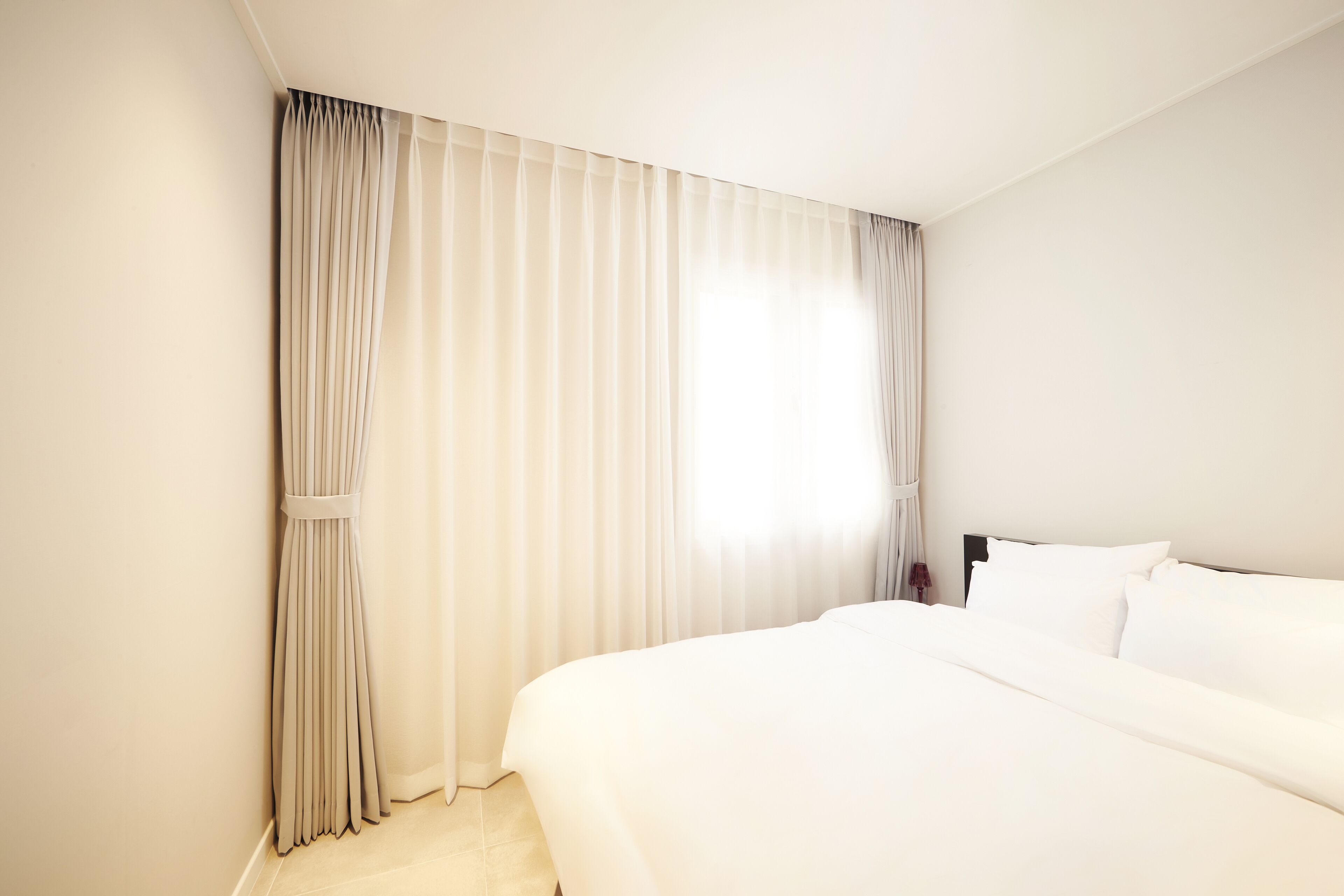A hotel room with a large bed, a nightstand, and a window with curtains.