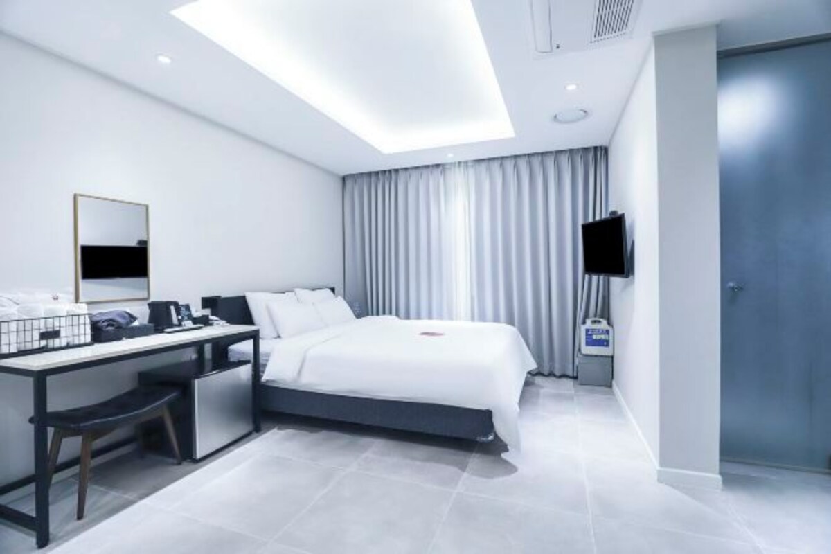 Ein modernes Hotelzimmer mit Bett, Schreibtisch, Stuhl, Flachbildfernseher und einem großen Fenster mit Vorhängen.