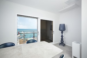 Una habitación con vista al mar, una mesa de comedor, sillas, una lámpara y un equipo de aire acondicionado blanco.