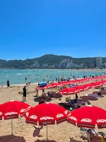 Una playa con sombrillas rojas y gente disfrutando del agua.